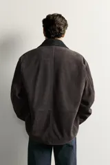 Cazadora de corte relaxed fit confeccionada en piel de ante de color marrón oscuro, con efecto lavado. Cuenta con cuello de solapa, manga larga, bolsillos frontales de parche y cierre frontal con botones.