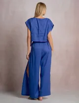 Pantalón palazzo de lino color azul, de tiro alto con cintura elastizada y cinto lazo incorporado con cuentas decorativas en las puntas. Presenta aberturas laterales pronunciadas en las piernas y corte amplio.