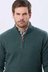 Buzo tejido de lana con cuello alto y medio cierre metálico frontal. Presenta un diseño de punto liso en color verde azulado con logo bordado en el pecho.