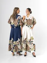 Conjunto de dos piezas confeccionado en viscosa con estampado floral en tonos marrones y verdes sobre base blanca. Incluye una blusa tipo camisa corta con cuello solapa, cierre frontal de botones y mangas abullonadas con diseño globo, y un pantalón tipo culotte de tiro alto, amplio y fluido con pinzas en la cintura.