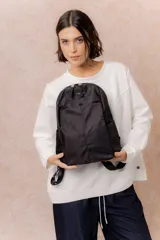 Mochila compacta de color beige, con compartimento principal con cierre, bolsillos laterales y bolsillo frontal con cierre oculto. Cuenta con correas regulables y acolchonadas y asa superior.