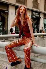 Chaleco sin mangas de cuero color marrón oscuro, con escote en V profundo y detalle de nudo o lazo en el centro del pecho. Presenta bolsillos de parche en la parte delantera.