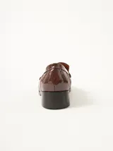 Mocasines de cuero negro con costuras pespunteadas en hilo blanco a contraste, diseño fruncido en la puntera, talón plano con pequeño tacón y apliques sutiles en charol.