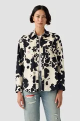 Camisa de manga larga con estampado de vaca en blanco y negro, cuello clásico y cierre de botones a presión. Incluye dos bolsillos frontales con solapa y un parche decorativo en el pecho.