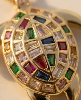 Cadena de eslabones finos con dije en forma de tortuga, con acabado dorado y detalles de circonias multicolor incrustadas en el caparazón.