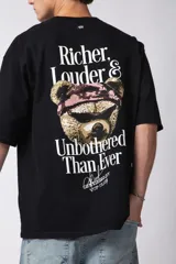 Remera de corte oversize color gris oscuro, confeccionada en algodón premium de alto gramaje. Presenta un diseño minimalista con un pequeño estampado frontal que incluye un oso y el texto 'Richer & Louder VCP'.