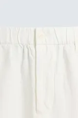 Pantalón de corte relajado confeccionado en tejido de cáñamo color blanco roto. Presenta cintura elástica con cordón interior ajustable, cierre frontal con botones, bolsillos laterales y un bolsillo trasero de plastrón.