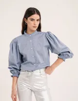 Blusa celeste de cuello mao y mangas abullonadas con puños elásticos. Tiene tajos laterales y botones en la delantera.