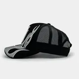 Gorra tipo trucker color negro con panel frontal bordado que presenta el logo 'LA' y diseño de llamas tribales en tonos gris y blanco. Cuenta con parte trasera de malla ajustable.