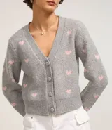 Cardigan corto gris con estampado de corazones rosas, escote en V y cierre abotonado.