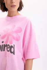 Remera oversize de manga corta en color rosado, con estampado gráfico frontal de una flor y la frase "Self Inspired" en tonos oscuros.