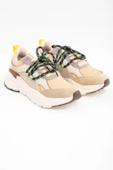Zapatilla urbana de diseño chunky, con paneles combinados en tonos beige, arena y gris. Presenta cordones jaspeados en azul y amarillo, tirador trasero amarillo y suela de plataforma dentada en color crema.