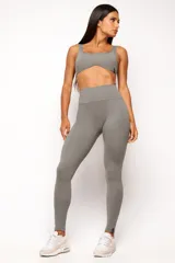 Conjunto deportivo de mujer color beige, compuesto por un top de tirantes anchos con escote curvado y calza de tiro alto con diseño sin costuras frontales.