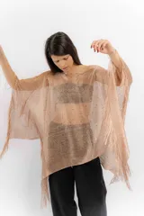 Poncho de tejido de punto metalizado en color dorado, con diseño amplio y flecos en el borde inferior. Presenta apliques sutiles de piedras y un estilo holgado.