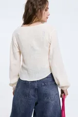 Camisa de algodón color crudo, de manga larga y corte fluido, con escote en V y cierre frontal mediante lazos.