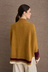 Buzo tejido de silueta amplia con cuello alto, mangas largas y puños en contraste. Presenta un diseño con franjas horizontales en el ruedo y detalles de tejido trenzado en las mangas.