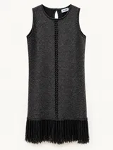 Vestido corto sin mangas de color negro, con diseño recto, cuello redondo y detalle de flecos en el dobladillo inferior. Presenta una línea vertical tejida al centro y un cierre de botón en la parte posterior del cuello.