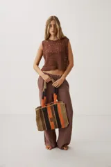Cartera tipo tote de diseño tejido a rayas, combinando tonos beige, marrón, negro y naranja. Cuenta con doble asa superior y detalle de etiqueta frontal.