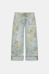 Jeans de tiro bajo confeccionados en denim, con diseño holgado y estampado integral de rosas en tonos amarillos y verdes sobre fondo celeste claro. Cuenta con cinco bolsillos, trabillas para cinto y botamangas con vuelta.