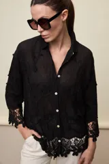 Camisa blanca de calce relajado, con cuello clásico, mangas 3/4 y cierre frontal de botones. Presenta bordados florales en relieve y detalles de crochet calado en los puños y el ruedo.