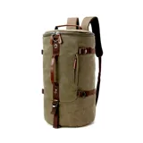 Bolso mochila de diseño cilíndrico confeccionado en tela canvas color verde oliva con detalles en cuero marrón. Cuenta con múltiples compartimentos, correas ajustables ocultables para usar como mochila, asas de mano y correa de hombro, con cierre vertical principal.
