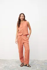 Pantalón de lino color ocre, de corte recto y tiro medio, con pinzas frontales y cierre de botón y cremallera.