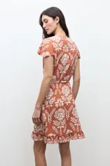 Vestido corto cruzado de color terracota con estampado floral blanco, escote en V, mangas cortas con vuelo y volados en el borde de la falda y la abertura.