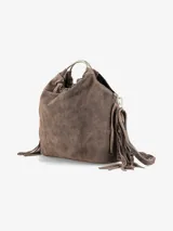 Cartera de mano confeccionada en cuero gamuzado color marrón, con diseño flexible y detalles de flecos laterales. Presenta un asa rígida metálica circular y una abertura superior fruncida.