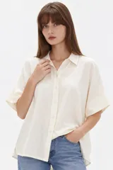 Camisa de viscosa color natural, de corte holgado, con cuello camisero, mangas cortas y cierre frontal con botones.