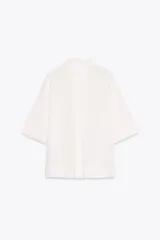 Camisa de color mostaza, con cuello solapa, manga corta y bajo recto. Cierre frontal con botones.