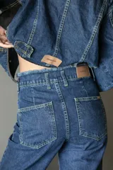 Pantalón de jean azul oscuro, de corte recto y tiro medio, con detalle de ruedo desflecado.