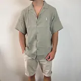 Camisa de hombre color verde oliva, de muselina con textura arrugada, manga corta, corte oversize, cuello cubano y cierre con botones. Presenta un pequeño logo bordado en el pecho.