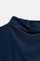 Vestido midi negro con cuello subido y diseño sin mangas (sisa). Presenta un elegante detalle de tejido drapeado en el lateral y cierre trasero con cremallera oculta.