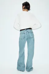 Jeans de tiro alto con diseño wide leg y cinco bolsillos. Presenta cierre frontal con cremallera y botón, e incluye un cinturón a contraste con hebilla metálica.