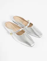 Mule tipo balerina color plateado, con punta fina y una tira decorativa sobre el empeine con un detalle de botón metálico dorado.