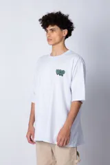 Remera de corte oversize color blanco, con cuello redondo y mangas cortas. Presenta un pequeño logo estampado en el pecho y un diseño gráfico grande en la espalda que incluye la frase 'Good Children' e ilustraciones de un ángel y llamas.