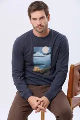 Remera de manga larga en color azul oscuro, con cuello redondo y estampado frontal de paisaje montañoso. Presenta un pequeño parche decorativo en la manga.