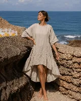 Vestido corto de lino color blanco, con mangas cortas amplias, escote redondo y diseño asimétrico más corto en la parte delantera y con volados en el ruedo.