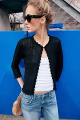 Chaqueta de punto calado con diseño pointelle, cuello redondo y manga larga. Presenta cierre frontal con corchete oculto y terminaciones con detalle de ondas en puños y ruedo.