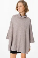 Sweater de tejido de punto en color beige, con cuello alto y diseño holgado de silueta amplia. Presenta mangas tres cuartos con puños doblados.