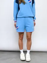 Short de felpa celeste, de corte deportivo, con detalles de pipings tricolor en los bordes y escudo del Club Nacional de Football aplicado en la pierna.
