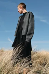 Chaqueta de punto con capucha, manga larga y cierre frontal con cremallera metálica. Presenta un diseño de tejido texturizado en color gris oscuro con detalles en contraste en los puños.