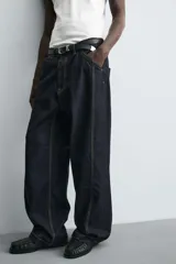 Jeans de denim oscuro, corte ancho (baggy fit) y tiro medio, con costura central girada en el frente de ambas piernas. Presenta pespuntes en color caramelo.