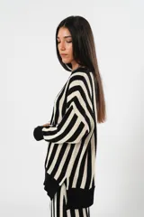 Saco oversize tejido a rayas verticales en blanco y negro, con escote en V y cierre frontal abotonado. Presenta puños y ruedo acanalados en color negro sólido.