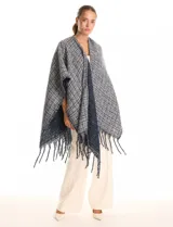Ruana de tejido tipo tweed en tonos azul y gris con destellos de lurex. Presenta un diseño abierto con terminaciones desmechadas y flecos en todo el borde inferior.