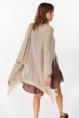 Ruana de punto color beige con diseño abierto y flecos en los bordes.