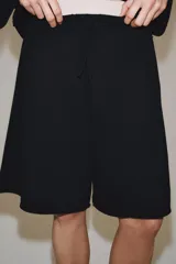 Bermuda de algodón color negro, con tiro medio, cintura elástica ajustable con cordones y bolsillos laterales ocultos en la costura.