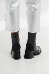 Bota corta de cuero negro con diseño bicolor que combina cuero liso y cuero charol en la puntera. Cuenta con taco cuadrado de altura media y cierre lateral interno.