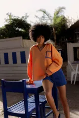 Buzo naranja de algodón con cuello en V y bordado en el frente. Tiene mangas largas con puños y ruedo acanalados.