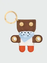 Llavero de cuero de la línea Les Champs Épuré de Longchamp en forma de figura con diseño de tótem, decorado con un pañuelo bandana celeste y detalles de tachas y argollas metálicas doradas grabadas. Cuenta con anilla metálica circular dorada.